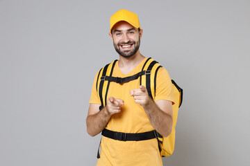 Delivery employee man guy male 20s in yellow cap t-shirt uniform thermal food bag backpack work courier service during quarantine coronavirus covid-19 virus, posing isolated on gray background studio.