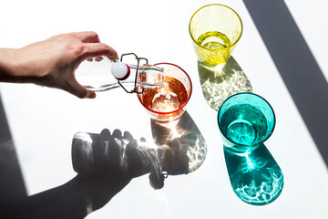 A person pours water into colored glass cups under the strong sunlight