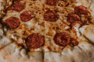A large round juicy mouth-watering pizza with cheese and salami lies on a cardboard box from a delivery package. paper backing. close view. see flour. good thin dough
