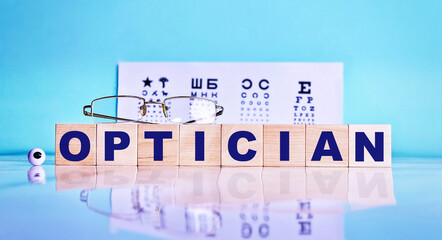 OPTICIAN word written on wooden cubes, glasses, eyes on the background of the vision test table....