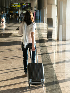 Woman walking with suitcase at the departure hall of the airport.