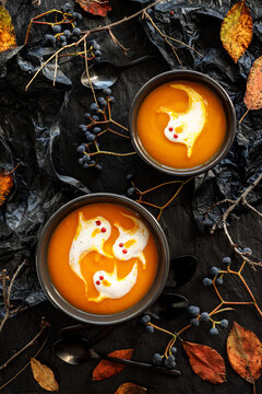 Halloween pumpkin soup decorated with cream ghosts in a black bowl top view