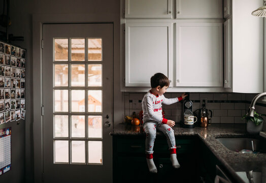 Young boy sitting on kitchen counter making coffee in morning time