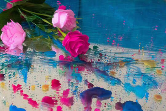Rosas rosadas sobre gotas de pintura de colores y espejo y fondo azul 