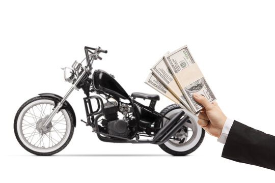 Male hand in front of a custom choper motorbike holding stacks of us dollar money