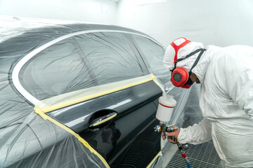 Automobile painting. Car painter with gun in chamber. Spray operation. 