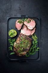 Traditional English barbecue lamb roast sliced with mint leaf and sauce offered as top view in a...