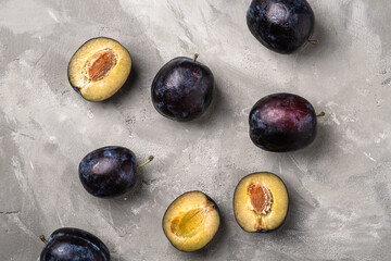 Fresh ripe plum fruits whole and sliced on stone concrete background, top view