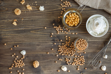 dry chickpea seeds, aquafaba broth and and whipped soft meringue in a bowl on a dark wooden table. Top view with space