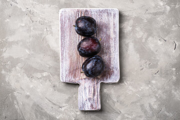 Fresh ripe plum fruits on wooden cutting board, stone concrete background, top view