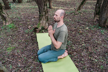 man doing sports yoga outdoors on the mat in the forest