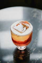 A beautiful pink cocktail with a big ice cube in a lowball glass, garnished with blood orange zest,...