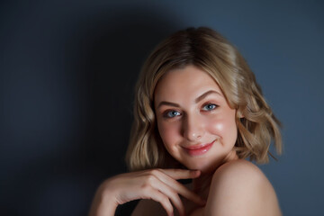 Close-up young pretty blonde woman smiles and flirts look against dark insulation background. Female emotion happy and actress of master. Concept of satisfaction and inspiration. Copyright space