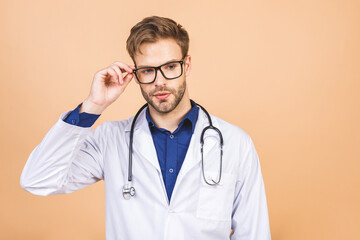 Portrait of cheerful smiling young doctor with stethoscope over neck in medical coat standing against isolated beige background.