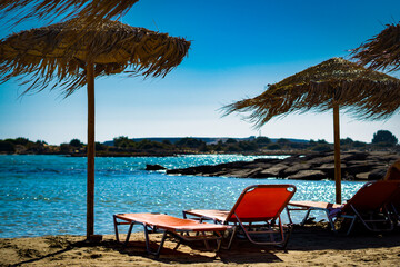 Beautiful mediterranean beach with empty sunbeds in the sand under sunshades with blue water and sky