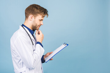 Happy smiling young doctor writing recipe on clipboard, isolated on blue background.