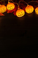Garland of halloween pumpkins on dark wooden background with copy space. Halloween background with glowing pumpkins and autumn maple leaves.