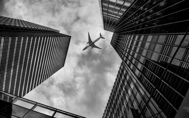 A airplane flies over modern buildings.