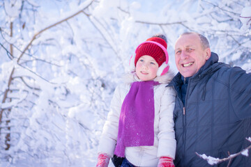 Winter family portrait of grandfather and granddaughter. A man and a little girl are smiling cheerfully against the background of a snow-covered forest.