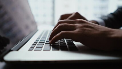 Close-up of hands of unrecognizable businessman typing on laptop keyboard while working at office desk on background of large panoramic window. Concept of office working. Tracking shot in slow motion. - Powered by Adobe