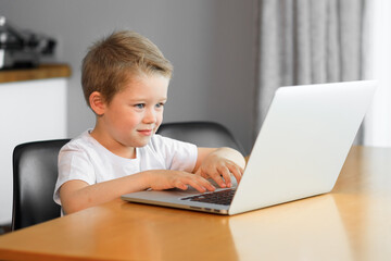 Funny young boy using a laptop computer sitting on top of a tableundefined at home