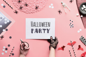 Halloween party text on white page held in hand. Flat lay with scissors and decorations on pink...