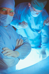 Group of surgeons at work in operating theater toned in blue. Medical team performing operation