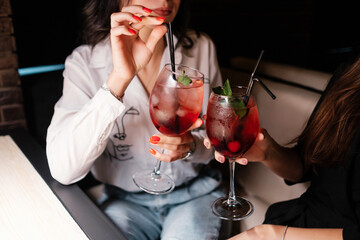Girls clinking glasses with cocktails. Cool party in full swing. Misted cocktail glasses with cherries and mint in the hands of lovely ladies.