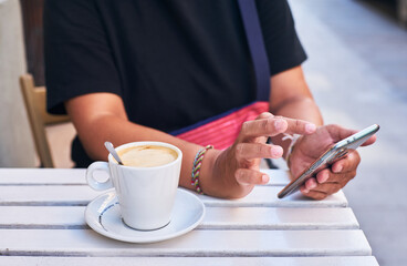 Fototapeta na wymiar Woman's hands using a mobile phone and having a coffee on a terrace