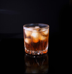 misted glass of whiskey with ice on black background