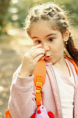 Walking girl in a pink jacket with an orange backpack in the autumn forest during leaf fall