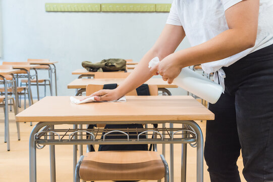 teacher disinfects classroom desk