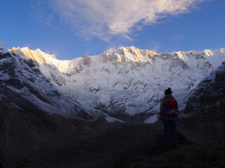 A mountain climber standing on a rock near the top and watches the sunrise over a snow-covered rock, ABC (Annapurna Base Camp) Trek, Annapurna, Nepal