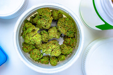 Top view of an open container of cannabis flower on a white background