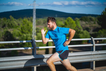 Young man takes a sprint over a highway bridge an hour before sunset surrounded by nature in Mallorca (Spain)