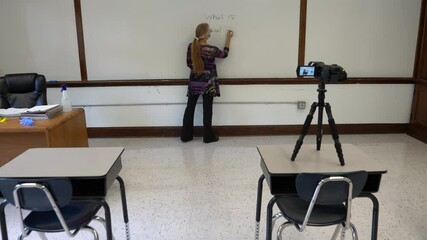 Camera pushes in on female civics or grammar teacher wearing medical face mask, writing what is racial equality on a white board in a school classroom. Concept posing question for students.