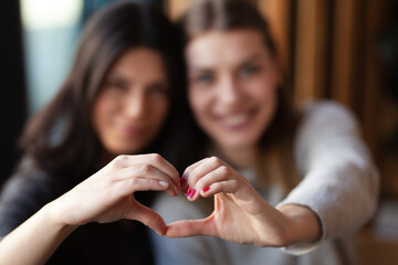 Two lovely girls smiling in a cafe and making a hearth shape with their hands.