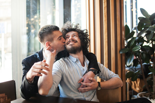 Two male friends in a cafe hugging and kissing on the cheek