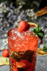 Strawberry Mojito. Cold summer mojito cocktail with strawberries, mint, lemon and ice in a glass on a table. on a dark background