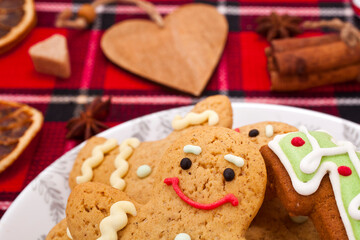 Gingerbread man with fir shaped cookies in a plate, dried orange slices and spices on a red fabric background. Christmas greeting card.