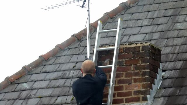 Man working on ladder installing digital television aerial on home roof
