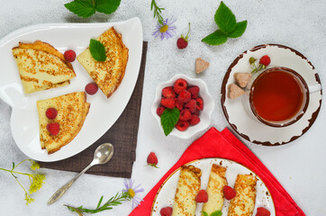 Pancakes with raspberries on a white ceramic plate in the shape of a heart. The concept of Shrovetide week and a pleasant tea party in the cozy atmosphere at home