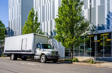 Big rig day cab white semi truck with box trailer for delivery and moving standing on the urban city street with multilevel residential apartments