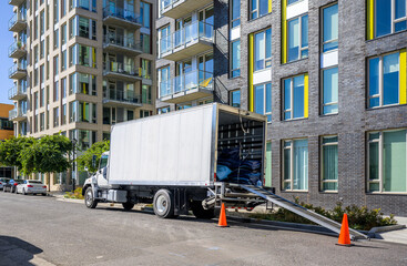 Naklejka premium Big rig semi truck unlloading cargo from box trailer with ladder standing on the urban city street with multilevel residential apartments buildings