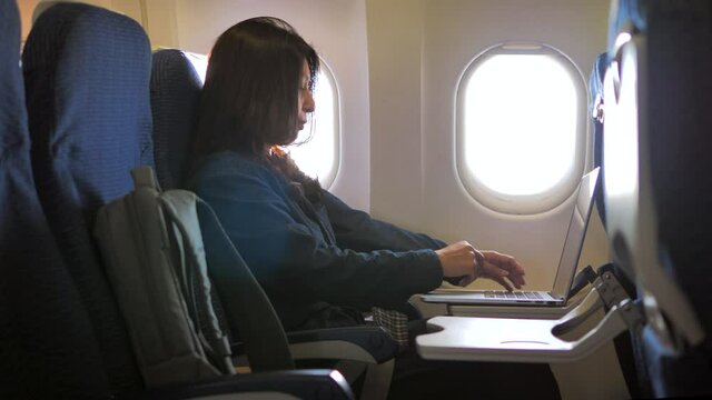 Side view of Businesswoman working on her laptop computer on board of an airplane during the flight 