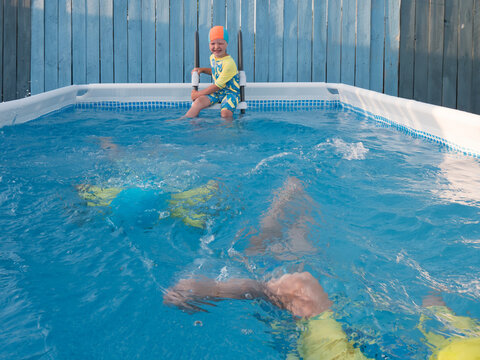 Cute boys in bathing suit swim and play in frame  swimming pool for country house. Children are happy together. Sunny summer day. concept of family vacations and active lifestyle after quarantine
