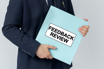 A businessman holds a folder with documents, the text on the folder is - FEEDBACK REVIEW