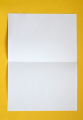 Folded white paper on yellow background .
