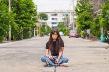 Close up portrait young Asian woman in a black T-shirt sitting on the floor holding a camera looking at the camera at the village road.