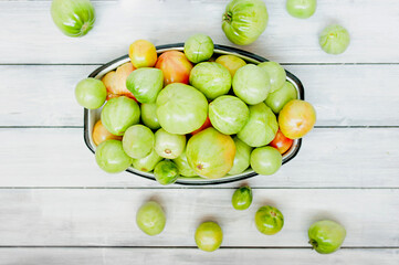 lot of green unripe tomatoes in metal Cup on light wooden background, top view, selective focus